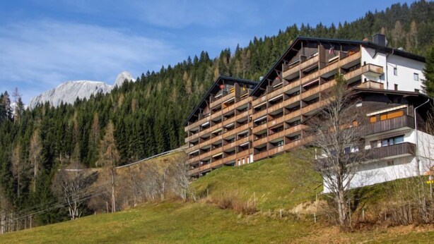 Ein mehrstöckiges Hotel mit Balkonen vor einer gebirgigen Landschaft.