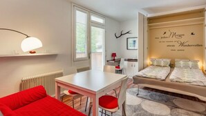 Ein modernes Zimmer mit Esstisch, einem roten Sofa und einem Bett mit gemustertem Überwurf.