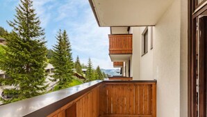 Ein Balkon mit Holzbalkonen, einem weißen Stuhl und Blick auf Bäume und Gebäude.