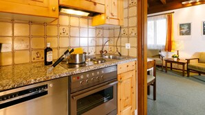 A kitchen with wooden cabinets, a granite countertop, stainless steel appliances, and a dining area with a table and chairs.