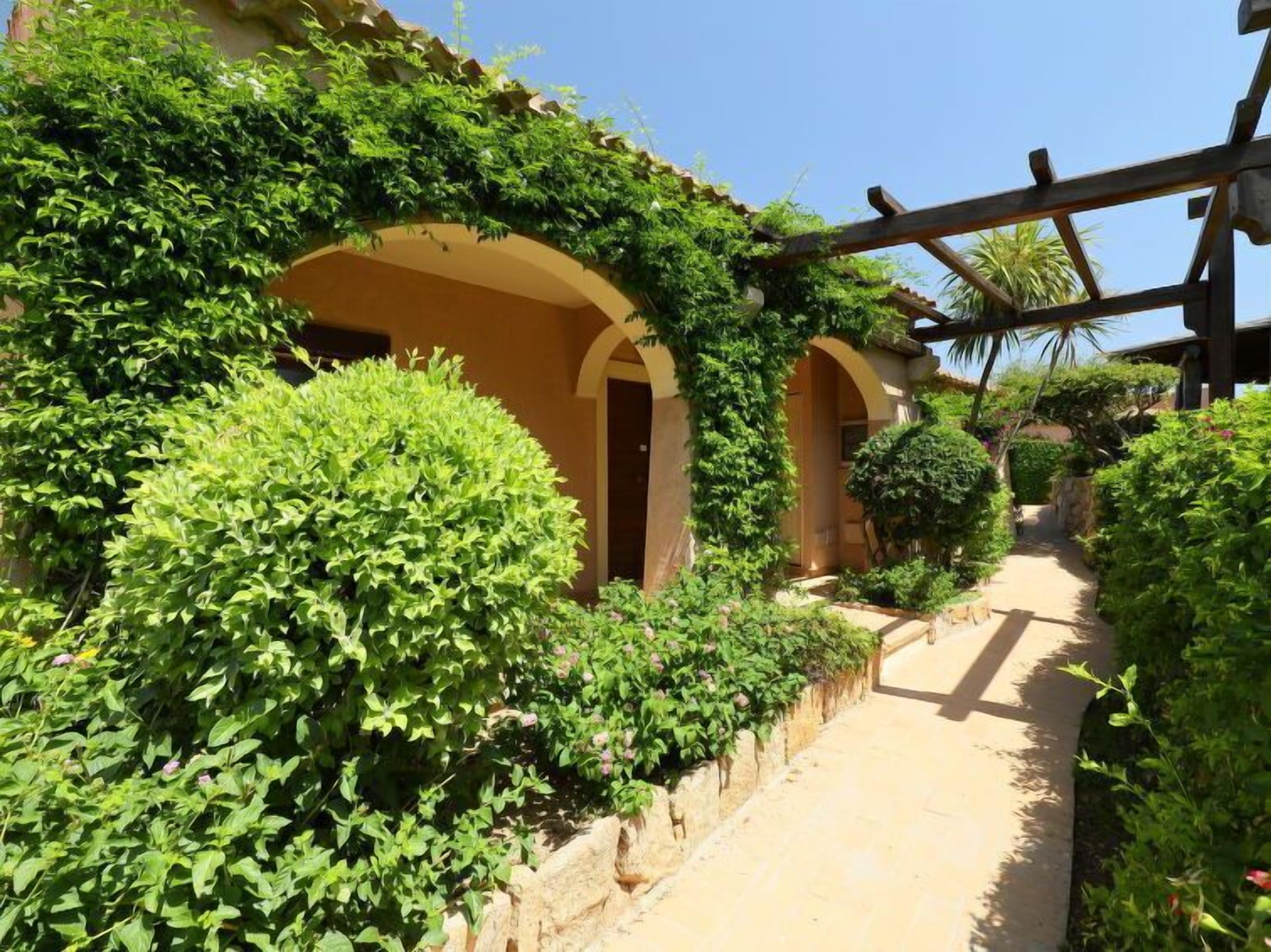 A pathway flanked by lush greenery and arched structures, suggesting a serene, garden-like setting.