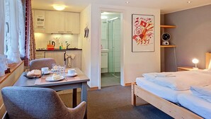 A hotel room with a bed, a dining table with breakfast items, a kitchenette, and a shower area. - Chalet Schwendihus by Interhome (Grindelwald)