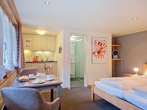 A hotel room with a bed, a dining table with breakfast items, a kitchenette, and a shower area. - Chalet Schwendihus by Interhome (Grindelwald)