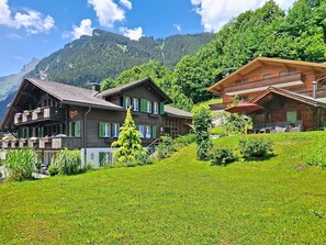 Un bâtiment de style chalet, doté de balcons, d’une façade en bois et surplombant une colline verdoyante.