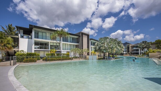 Un hôtel moderne doté d’une grande piscine, de palmiers et surplombant un ciel d’un bleu éclatant.