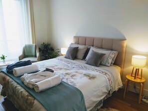 Un lit bien fait, recouvert d’une couvre-lit à motifs floraux, agrémenté de plusieurs oreillers et de serviettes pliées posées sur une table de chevet.