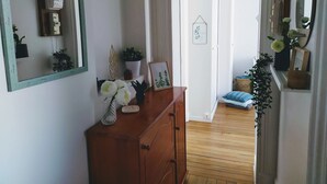 Ein Zimmer mit einem hölzernen Schminktisch, einem Spiegel und einer Tür zu einem weiteren Raum, der ein Bett und eine kleine Pflanze beherbergt.