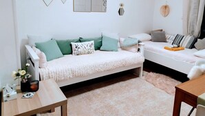 Ein gemütliches Wohnzimmer mit einem weißen Sofa, grünen Kissen, einem kleinen Holztisch und einem flauschigen Teppich.