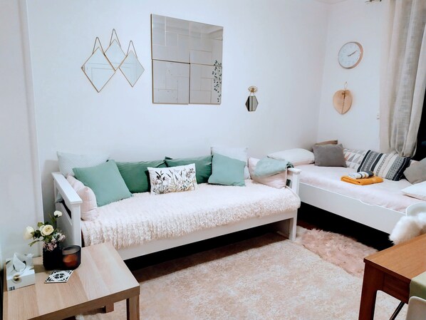 Un salon chaleureux avec un canapé blanc, des coussins verts, une petite table en bois et un tapis moelleux.