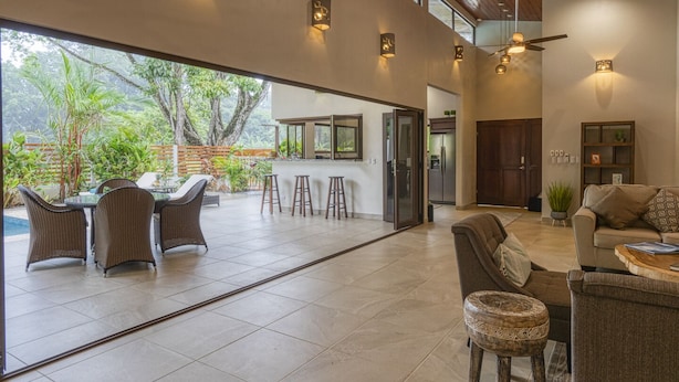 A spacious living area with a large glass door leading to an outdoor patio, furnished with wicker chairs and a bar area. - Sleeps 8, Brand New, private pool, steps from beach, dining and shopping (Dominical)