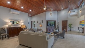 A spacious living room with a large sofa, a dining area with a table and chairs, and a kitchen area with cabinets and a countertop. - Sleeps 8, Brand New, private pool, steps from beach, dining and shopping (Dominical)