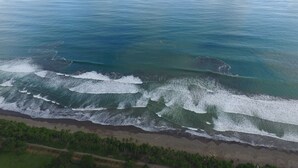 An aerial view of a beach with waves crashing onto the shore, surrounded by greenery. - Sleeps 8, Brand New, private pool, steps from beach, dining and shopping (Dominical)