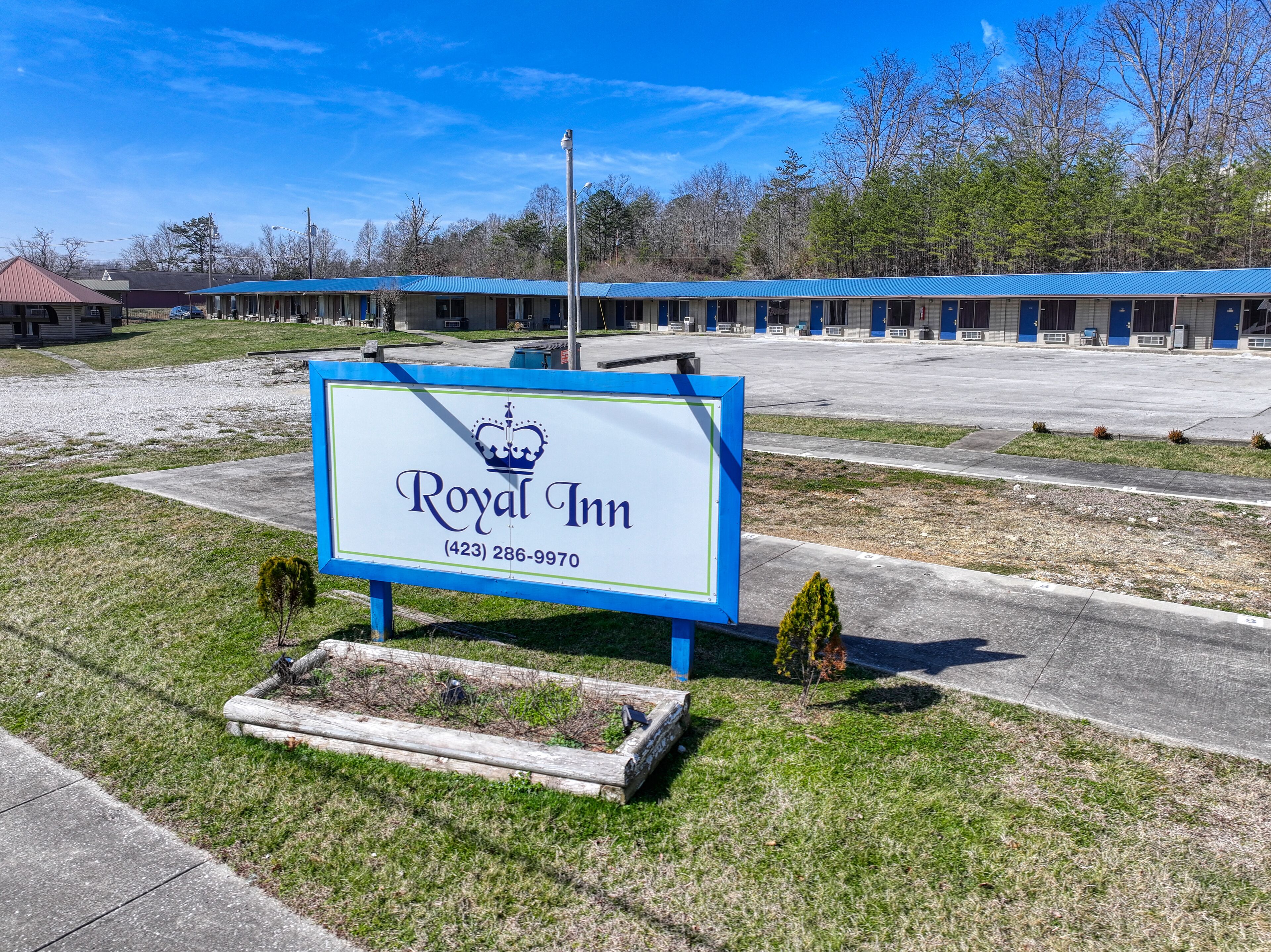 A Royal Inn sign with a contact number, set against a backdrop of a motel with blue roofs and a parking lot.
