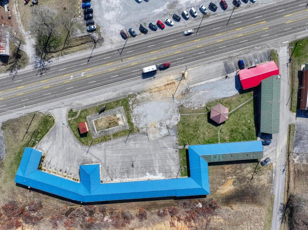 An aerial view of a parking lot with multiple cars, a large blue-roofed building, and a red-roofed structure.