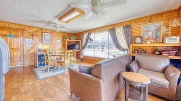 Una habitación acogedora con detalles de madera, un ventilador de techo, un televisor, un sofá, una mesita y una ventana con cortinas.