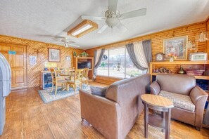 A cozy room with a wooden interior, a ceiling fan, a television, a sofa, a small table, and a window with curtains.