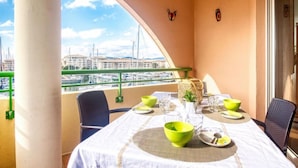 En balkon med et bord dækket til to, med udsigt over en lysthavn med både og bygninger.