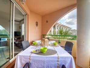 Een balkon met een eettafel, stoelen, een televisie en uitzicht op palmbomen en gebouwen.