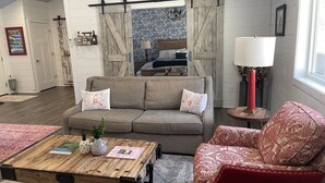 A living room with a sofa, a red armchair, a wooden coffee table, and a chandelier. - Cute cabin in our private woods, close to a bike trail, winery, and lakes (Traverse City)