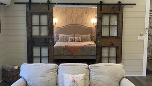 Un dormitorio acogedor con cama, una puerta corrediza estilo granero, un sofá y una mesa de centro tejida.