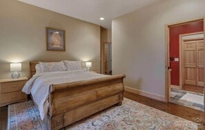 Une chambre à coucher avec un lit en bois, deux tables de chevet avec des lampes, un tapis à motifs et une porte avec un cadre rouge.