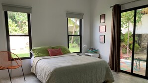 Un dormitorio con cama, una silla, una mesita de noche y una ventana con vistas a zonas verdes.