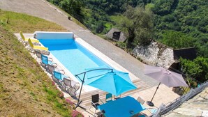 Ein Pool mit Liegestühlen und Sonnenschirmen, umgeben von einer hügeligen Landschaft.