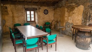 A rustic room with a long wooden table, green chairs, a dartboard, and a small round table.