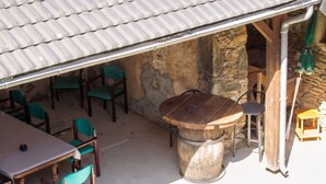 An outdoor seating area with a stone wall, wooden chairs, and a large wooden table.