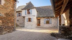 A traditional stone building with a gravel courtyard, wooden shutters, and a sloped roof. - Homerez - Villa in Vieillevie + private pool (Vieillevie)