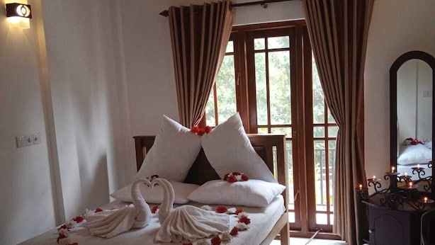 A neatly made bed with a swan design and rose petals, a wooden bench, a mirror, and a window with curtains. - White House Holiday Home (Maspotha)
