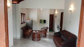A spacious living area with a sofa, wooden chairs, a TV, and a refrigerator. - White House Holiday Home (Maspotha)