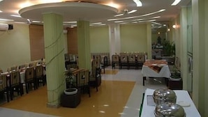 A dining area with rows of tables and chairs, a central table with a tablecloth, and a ceiling with circular light fixtures. - Hotel Galaxy (Dehradun)