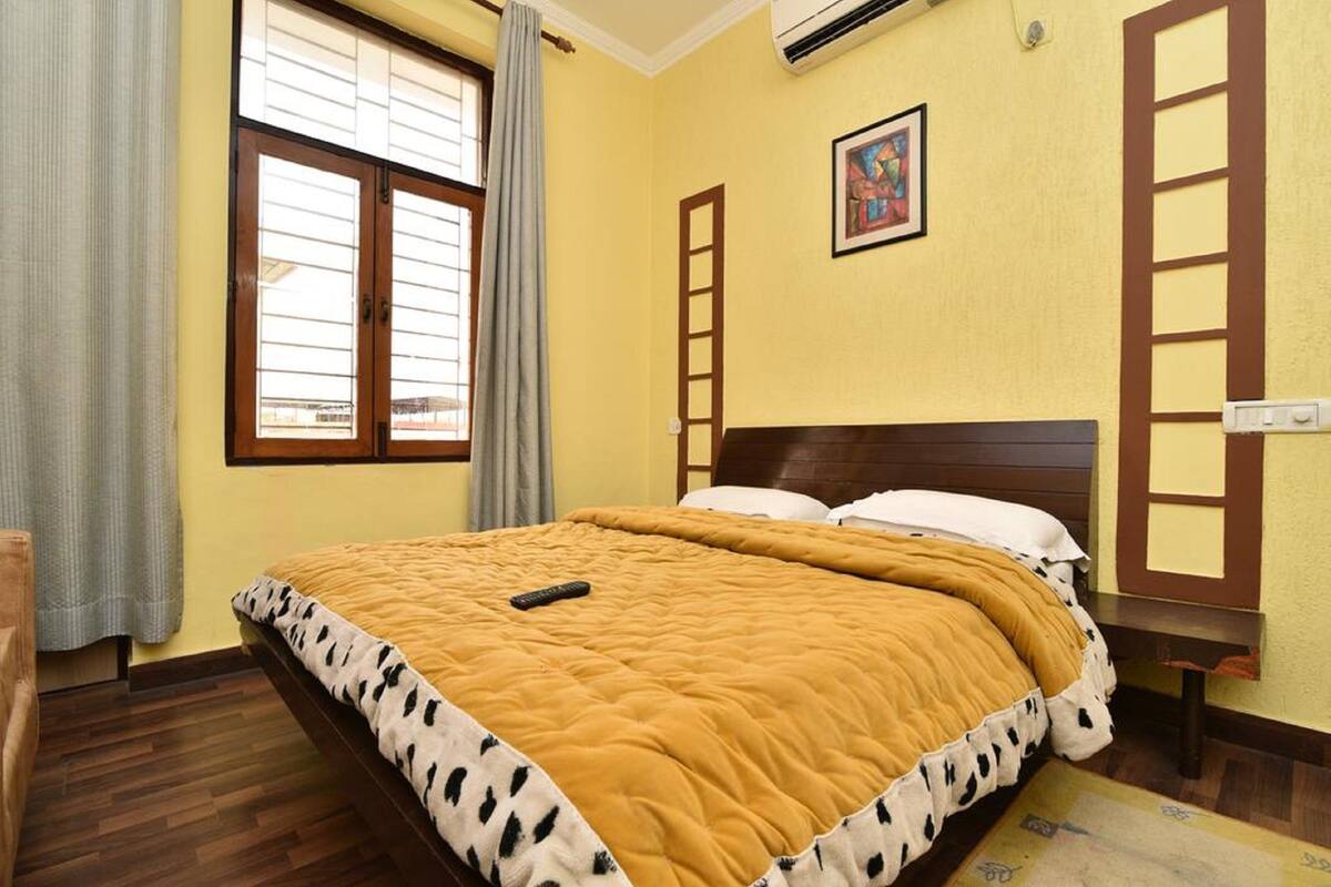 Un dormitorio con cama, ventana con cortinas, escalera y un cuadro en la pared.