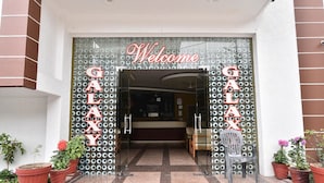 A hotel entrance with a 'Welcome' sign and 'GALAXY' letters on the wall. There are potted plants and a chair outside. - Hotel Galaxy (Dehradun)