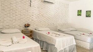 A hotel room with two beds, a brick-patterned wall, an air conditioning unit, and two framed pictures. - Pousada La Goduria (Aracati)
