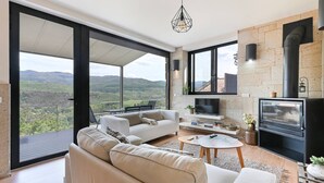 A spacious living room with a large sofa, a coffee table, and a fireplace. There is a television and a stone wall. - Casas das Olas - House 5 (Arcos de Valdevez)