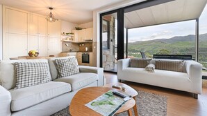 A modern living room with two sofas, a coffee table, and a kitchen area with a view of the countryside. - Casas das Olas - House 5 (Arcos de Valdevez)