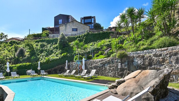 A swimming pool with lounge chairs and umbrellas, surrounded by greenery and a stone wall. - Casas das Olas - House 5 (Arcos de Valdevez)