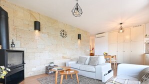 A modern living room with a stone wall, a fireplace, a white sofa, a coffee table, and a dining area with a table and chairs. - Casas das Olas - House 5 (Arcos de Valdevez)