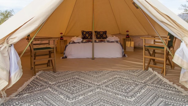 Ein großes Zelt mit einem Bett, zwei Stühlen und einem gemusterten Teppich.