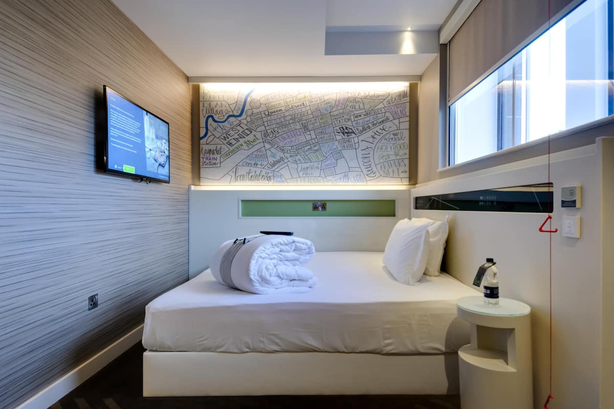 Habitación de hotel con cama, televisor de pantalla plana, mapa en la pared, una mesita con una botella y ventana.