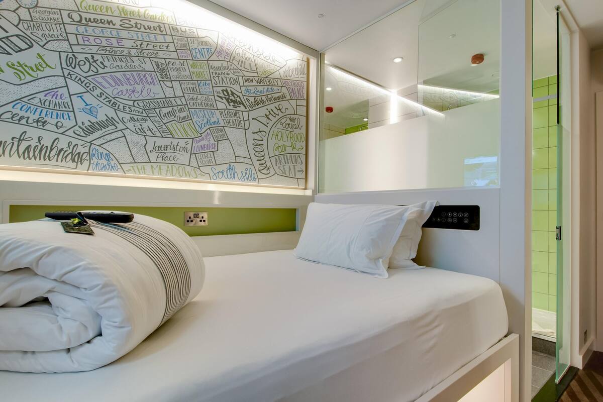 Habitación de hotel con una cama bien hecha, un mapa mural y un panel de control en la cabecera.