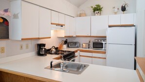 Una cucina moderna con mobili bianchi, un lavello in acciaio inossidabile, un fornello, una macchina da caffè, un tostapane e un frigorifero.
