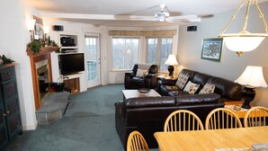 A living room with a fireplace, a television, a sofa, a dining table, and a ceiling fan.