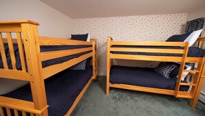 A room with two wooden bunk beds, each with a mattress and pillows. The room has a patterned wallpaper and a carpeted floor.