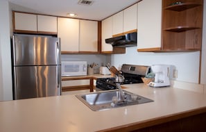Compact kitchen with modern appliances and cabinetry, featuring a refrigerator, microwave, stove, kettle, and coffee maker.