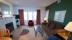 A living room with a fireplace, a brown sofa, a red armchair, a blue couch, and a dining table with chairs. - Ski-In/Ski-Out Condo with Access to Indoor Pool (Ludlow)