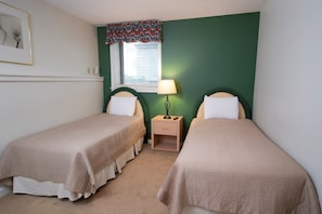 Cozy bedroom with two single beds, a nightstand, and a window with a decorative valance.