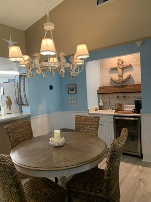 A dining area with a round table, wicker chairs, a chandelier, and nautical-themed wall decor.